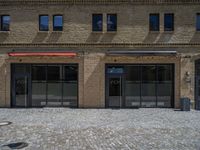 the sidewalk is paved with stones and has a bench in front of it, with no people inside