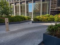 the side walk of a glass office building with concrete bricks and landscaping on each floor