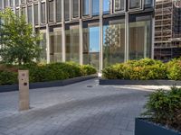 the side walk of a glass office building with concrete bricks and landscaping on each floor