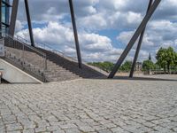 a person on a bike walking through a stone building entrance, in front of an enormous glass wall and stairs