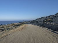 a motorcycle that is sitting on a dirt road near some rocks and the ocean at the top of a hill