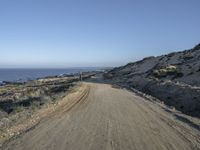 a motorcycle that is sitting on a dirt road near some rocks and the ocean at the top of a hill