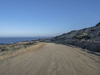 a motorcycle that is sitting on a dirt road near some rocks and the ocean at the top of a hill