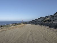 a motorcycle that is sitting on a dirt road near some rocks and the ocean at the top of a hill