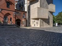 cobblestone driveway surrounded by modern buildings on sunny day with sun reflecting onto the windows