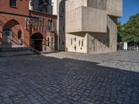 cobblestone driveway surrounded by modern buildings on sunny day with sun reflecting onto the windows