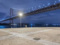 the night scene of a large suspension bridge and some lights are seen in the foreground