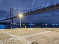 the night scene of a large suspension bridge and some lights are seen in the foreground