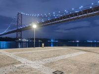 the night scene of a large suspension bridge and some lights are seen in the foreground