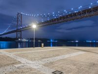 the night scene of a large suspension bridge and some lights are seen in the foreground