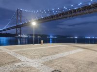 the night scene of a large suspension bridge and some lights are seen in the foreground