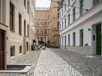 a cobblestone street between buildings in europe with a grate in the middle