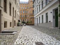 a cobblestone street between buildings in europe with a grate in the middle