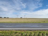 a grassy area with power lines, road, and road sign in front of grass