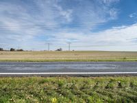 a grassy area with power lines, road, and road sign in front of grass