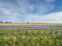 a grassy area with power lines, road, and road sign in front of grass