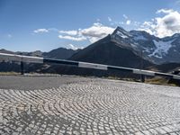 a rail near the side of a mountain on a sunny day with snow covered mountains in the background