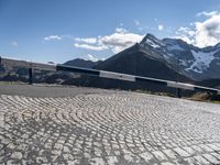 a rail near the side of a mountain on a sunny day with snow covered mountains in the background