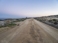 a dirt road with some hills behind it and the ocean in the distance and the sky