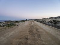 a dirt road with some hills behind it and the ocean in the distance and the sky