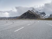 the road has two winding lines and snow covered mountains in the background of the photo