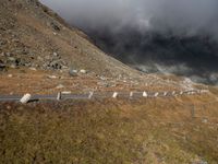 the sky is cloudy over a mountain with clouds in it, and sheep on the ground