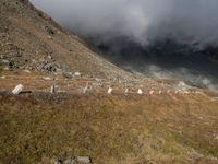 the sky is cloudy over a mountain with clouds in it, and sheep on the ground