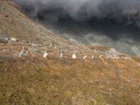 the sky is cloudy over a mountain with clouds in it, and sheep on the ground