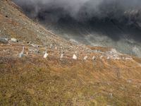 the sky is cloudy over a mountain with clouds in it, and sheep on the ground