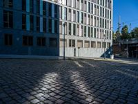 a brick sidewalk and some buildings and a street light on a sunny day, with shadows