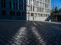 a brick sidewalk and some buildings and a street light on a sunny day, with shadows