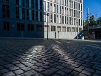 a brick sidewalk and some buildings and a street light on a sunny day, with shadows