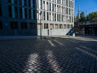 a brick sidewalk and some buildings and a street light on a sunny day, with shadows