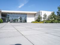 a photo of the exterior of a large white building with many windows, trees, bushes and stone flooring