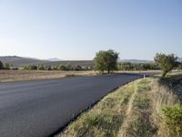 an empty country road near a hilly plain of land and grass to the side of it