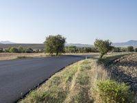 an empty country road near a hilly plain of land and grass to the side of it