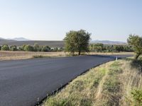 an empty country road near a hilly plain of land and grass to the side of it