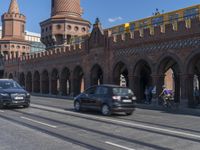 several cars and cars driving in traffic near a brick wall and a clock tower at an intersection