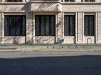 a man walking along a street past a brick building with windows and a fire hydrant