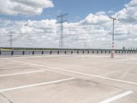 an empty parking lot with several electric towers above it and water below in the distance