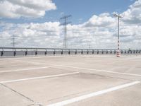 an empty parking lot with several electric towers above it and water below in the distance