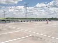 an empty parking lot with several electric towers above it and water below in the distance