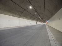 two people walking inside the tunnel of a highway with no lanes, a long empty street next to them