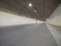 two people walking inside the tunnel of a highway with no lanes, a long empty street next to them