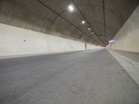 two people walking inside the tunnel of a highway with no lanes, a long empty street next to them