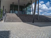 a person on a bike walking through a stone building entrance, in front of an enormous glass wall and stairs