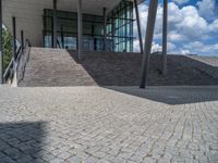 a person on a bike walking through a stone building entrance, in front of an enormous glass wall and stairs