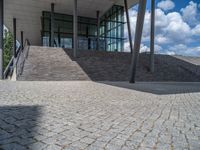 a person on a bike walking through a stone building entrance, in front of an enormous glass wall and stairs