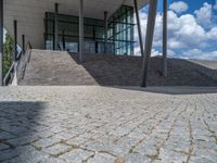 a person on a bike walking through a stone building entrance, in front of an enormous glass wall and stairs