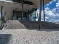 a person on a bike walking through a stone building entrance, in front of an enormous glass wall and stairs